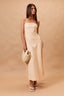 Woman wearing a strapless beige dress holding a woven bag against a beige background