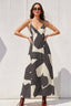 Woman wearing a black and white patterned dress against a white wall.