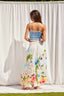Woman wearing a blue top and floral skirt against a white curtain backdrop