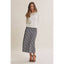 A woman modeling a white knit sweater and a navy and white plaid midi skirt, paired with black strappy heels, against a solid light beige studio background.