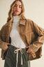 A woman wearing an oversized brown corduroy utility jacket over a white turtleneck and dark green drawstring pants, photographed against a plain light beige studio background.