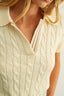 Close-up of a person wearing a cream-colored cable knit sweater against a neutral background