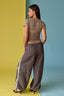 Woman wearing a patterned top and gray pants with white stripes on a two-tone yellow and blue background