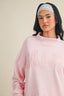 Woman wearing a pink sweatshirt with 'GALY' text and a striped headband on a beige background