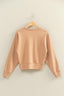 Beige sweatshirt on a wooden hanger against a beige wall