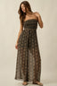 Woman wearing a strapless, long, patterned dress against a plain background