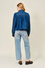 Person wearing a blue denim jacket and jeans on a plain background