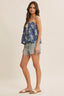 Woman wearing a blue floral top and denim shorts on a beige background
