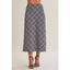 A model wearing a navy plaid midi skirt with black strappy high-heeled sandals, shown from the waist down against a solid beige background.