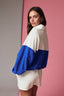 Woman wearing a white and blue color-blocked sweater against a pink wall.