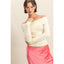 Woman wearing a white off-shoulder sweater and pink skirt against a plain background