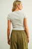 Person wearing a white ribbed top and green pleated pants against a plain background