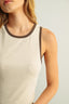 Close-up of a person wearing a beige tank top with brown trim on a light background