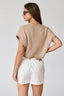 Woman wearing a beige ribbed sweater and white shorts on a plain background