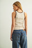 Woman wearing a beige tank top and blue jeans against a plain background