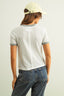 Person wearing a white textured shirt with gray trim and blue jeans, standing against a plain background.