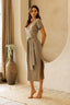 Woman wearing a gray dress standing in a room with a large vase and plant.