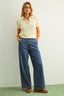Woman wearing a light yellow sweater and blue jeans against a white background