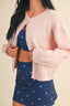 Person wearing a pink cardigan over a navy blue outfit with white patterns on a beige background