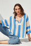 Woman wearing a blue and white striped crochet poncho sitting on a white surface.