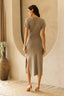 Woman wearing a beige dress standing in a room with a textured wall and decorative vase.