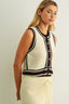 Woman wearing a sleeveless crochet top with black and white pattern on a plain background