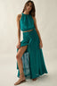 Woman wearing a teal outfit with a halter top and long skirt on a plain background