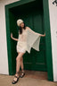 Woman in a white dress and hat standing in front of a green door.