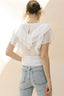 Person wearing a white blouse with ruffled details and light blue jeans against a neutral background