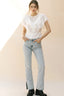 Woman wearing a white ruffled blouse and light blue jeans against a beige background