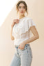 Woman wearing a white ruffled blouse and light blue jeans against a beige background