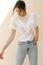 Woman wearing a white ruffled blouse and light blue jeans against a beige background