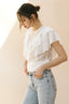 Woman wearing a white ruffled blouse and light blue jeans against a beige background