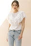 Woman wearing a white ruffled blouse and light blue jeans against a beige background