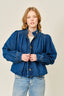Woman wearing a blue denim jacket and jeans on a beige background