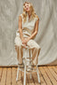 Woman sitting on a stool wearing a beige outfit against a plain background