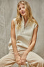 Woman wearing a beige sleeveless top and pants sitting on a stool against a neutral background