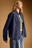 Woman wearing a navy jacket over a striped shirt on a brown background