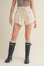 Person wearing a white skirt and black rain boots on a beige background