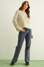 Woman wearing a beige sweater and blue jeans against a light green background