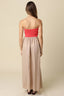 Woman wearing a strapless red top and beige skirt on a beige background