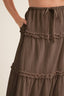 Close-up of a brown crinkled tiered skirt with ruffled trim and a drawstring waist, shown on a model against a light neutral background.