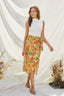 Woman wearing a white top and colorful floral skirt against a white curtain background.