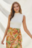 Woman wearing a white sleeveless top and colorful floral skirt against a neutral background