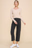 Woman wearing a beige sweater and black jeans against a beige background