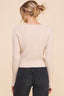 Person wearing a beige sweater and black pants against a beige background