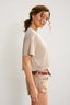Woman wearing a beige shirt and shorts on a plain background