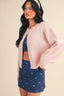 Woman wearing a pink cardigan over a blue outfit with a white pattern on a beige background