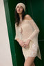 Woman wearing a beige crochet cover-up and headscarf against a green door.