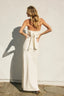 Woman in a white dress standing against a plain wall with a soft shadow on the ground.
